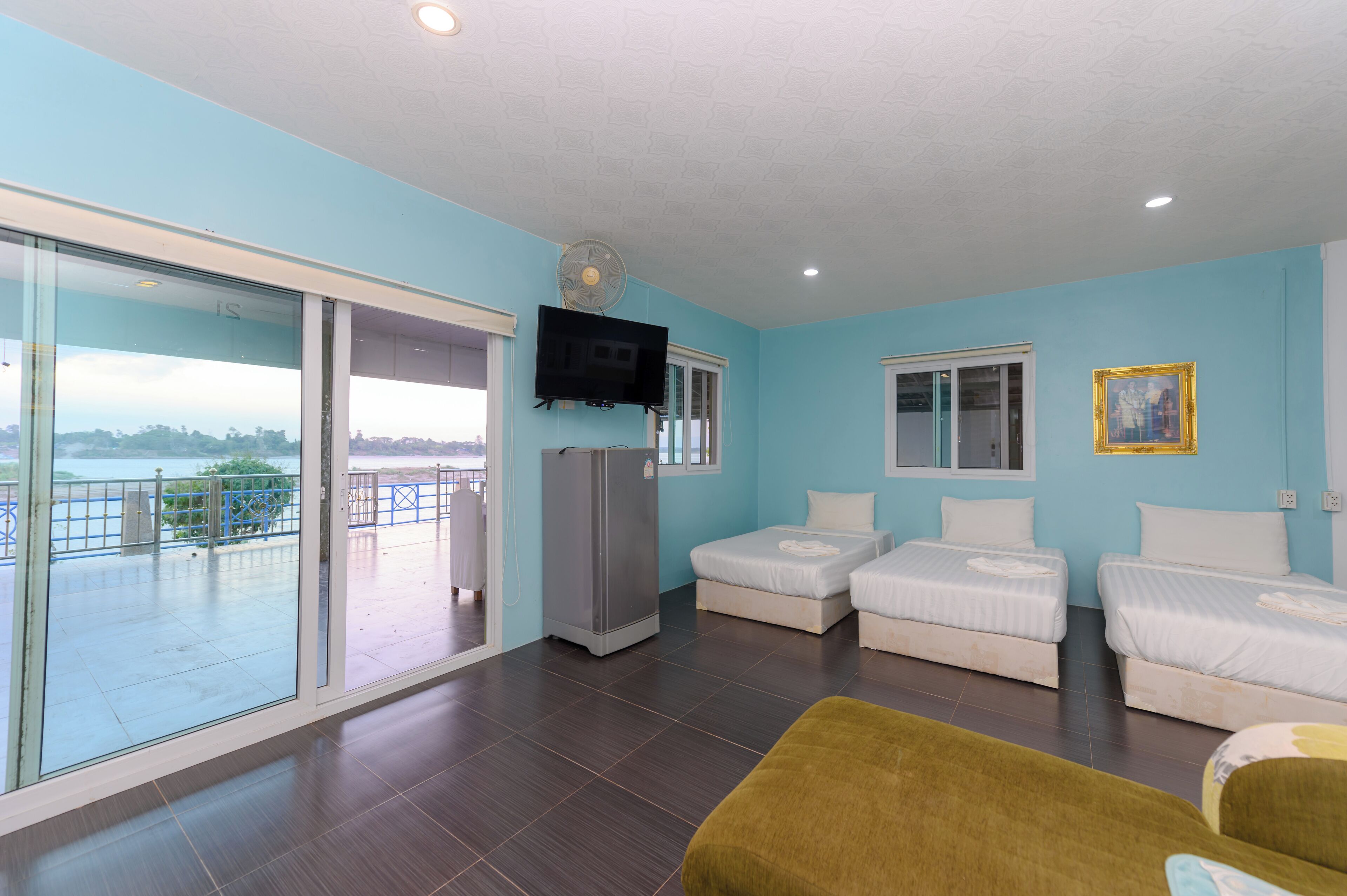 A room with two beds, a TV, a refrigerator, and a sliding glass door to a balcony.