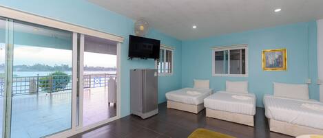 A room with two beds, a TV, a refrigerator, and a sliding glass door to a balcony.