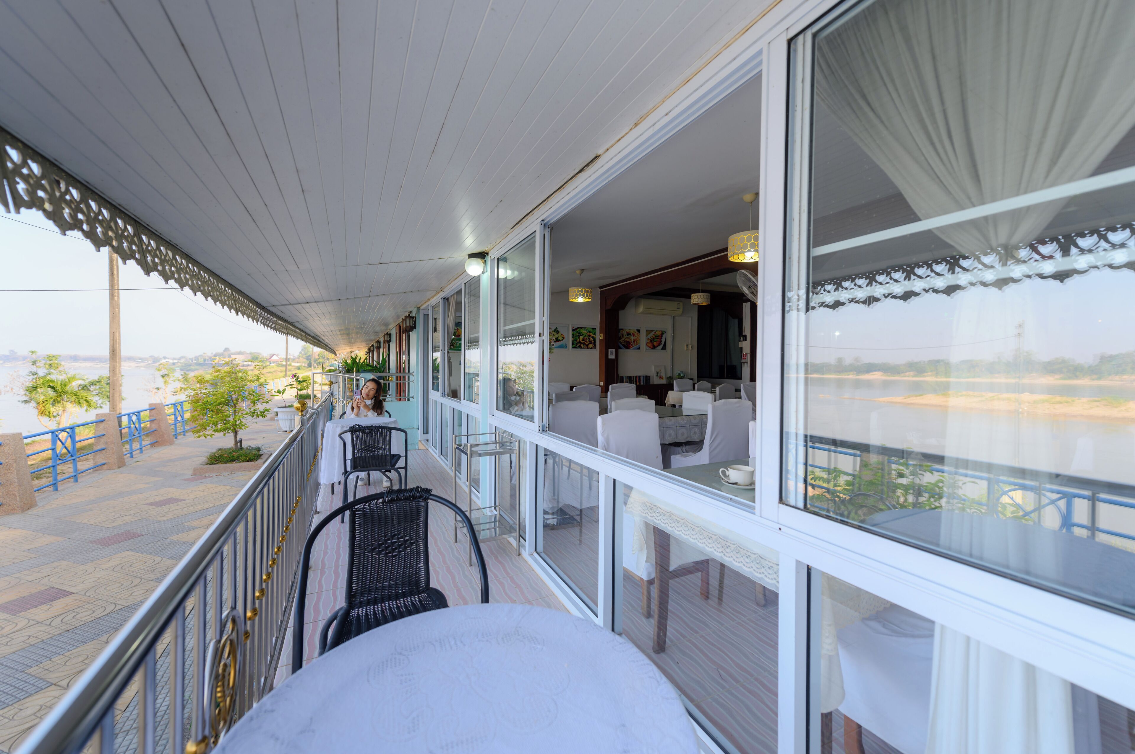 A covered outdoor seating area with tables and chairs, overlooking a body of water.