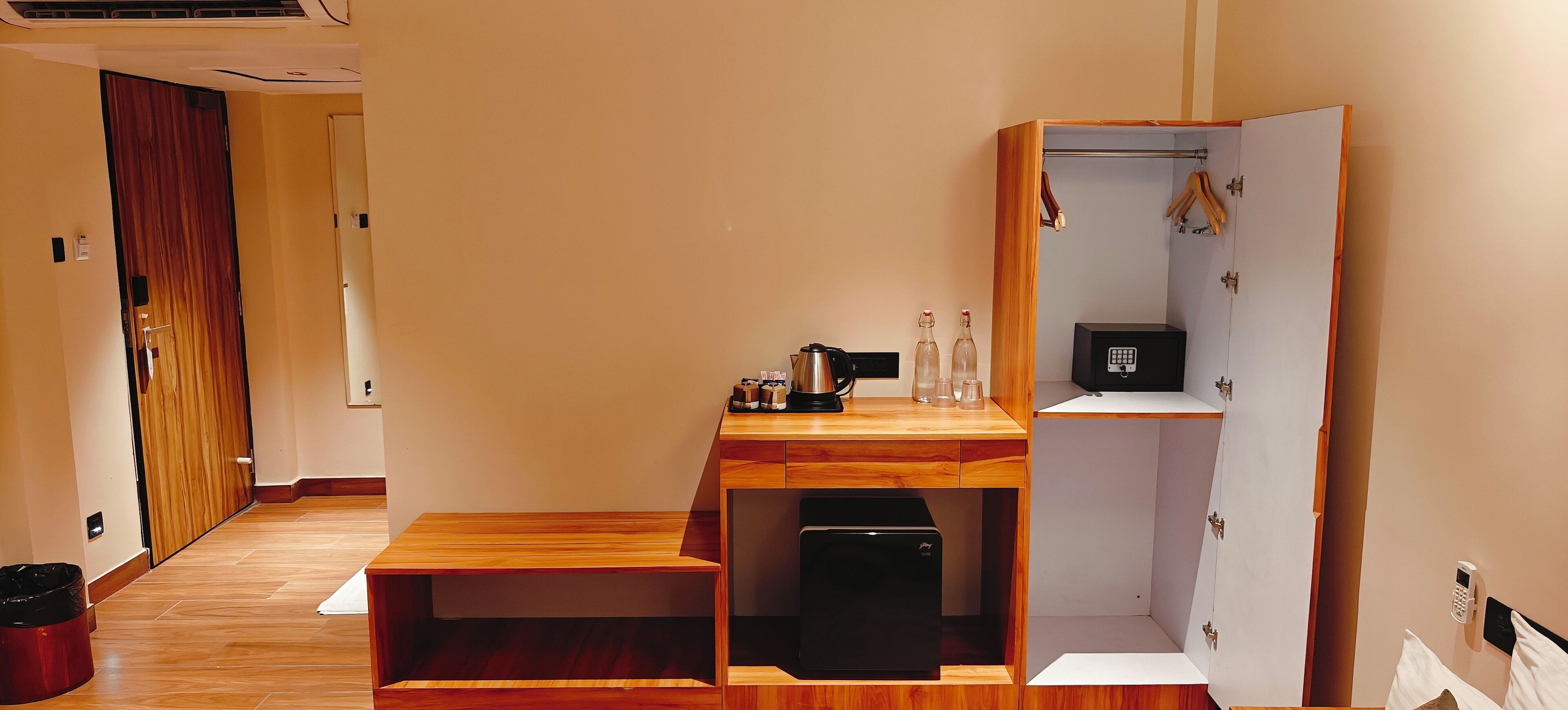 Habitación compacta con un escritorio de madera, un refrigerador pequeño negro y un armario con perchero.
