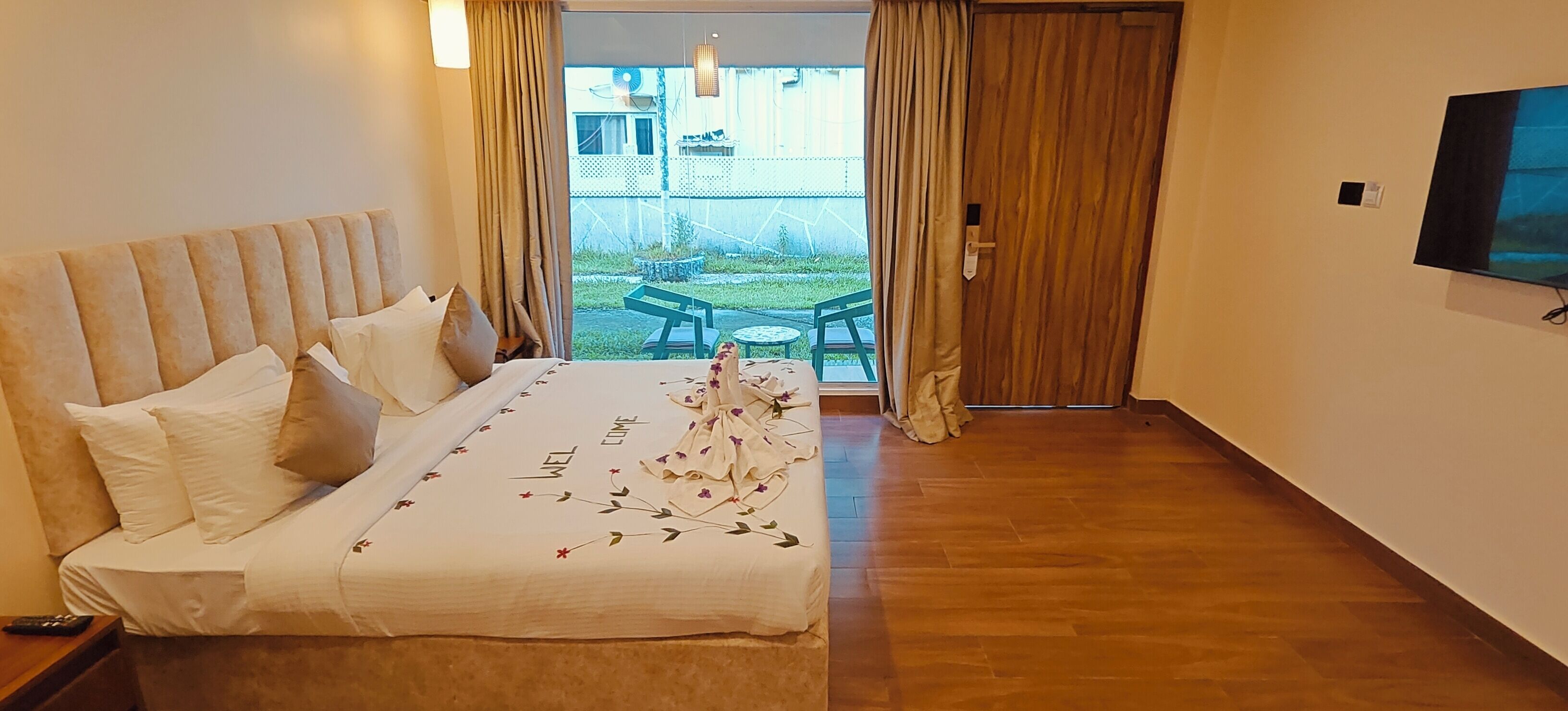 A hotel room with a large bed, a TV on the wall, and a view of the outdoor area through a sliding door.