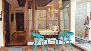 A hotel entrance with numbered doors, a glass partition, and teal chairs by a small round table. - ARINA ISLAND RESORT-A BERGAMONT GROUP (Port Blair)