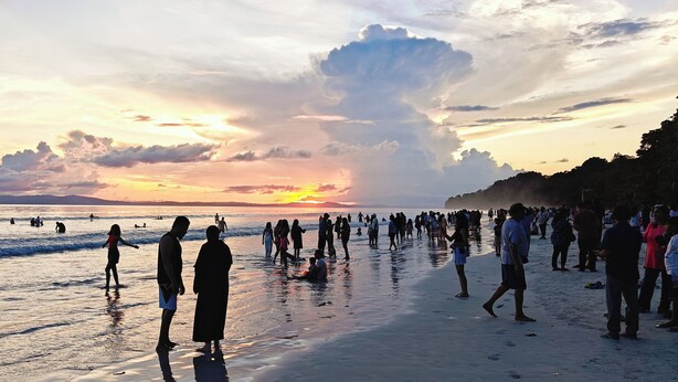 A crowded beach at sunset with people walking and standing in the water. - ARINA ISLAND RESORT-A BERGAMONT GROUP (Port Blair)