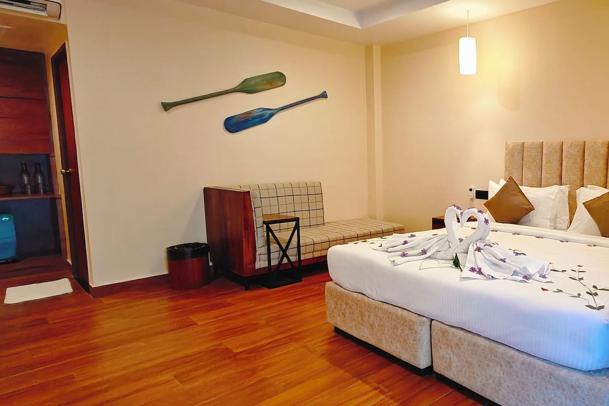 A hotel room with a large bed, a wooden floor, a small desk with a phone, and a wall-mounted TV.
