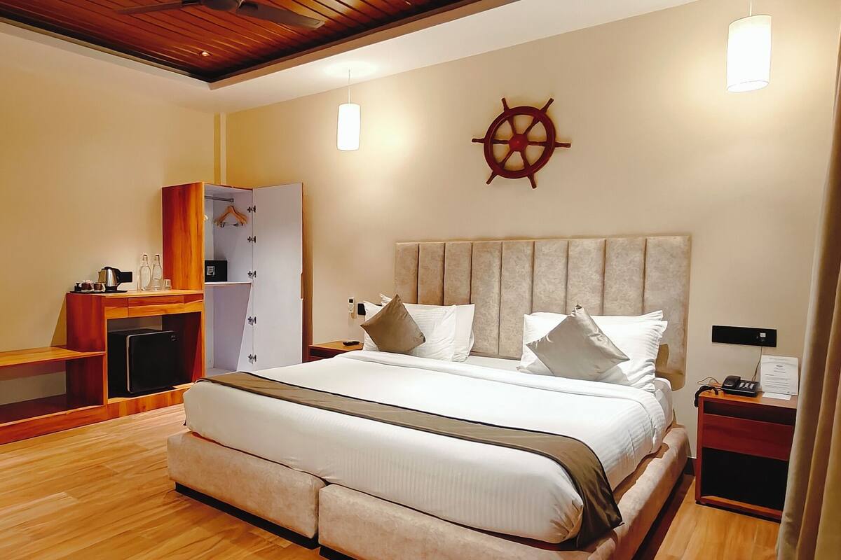 A hotel room with a large bed, a wardrobe, a desk, and a ship's wheel decoration on the wall.