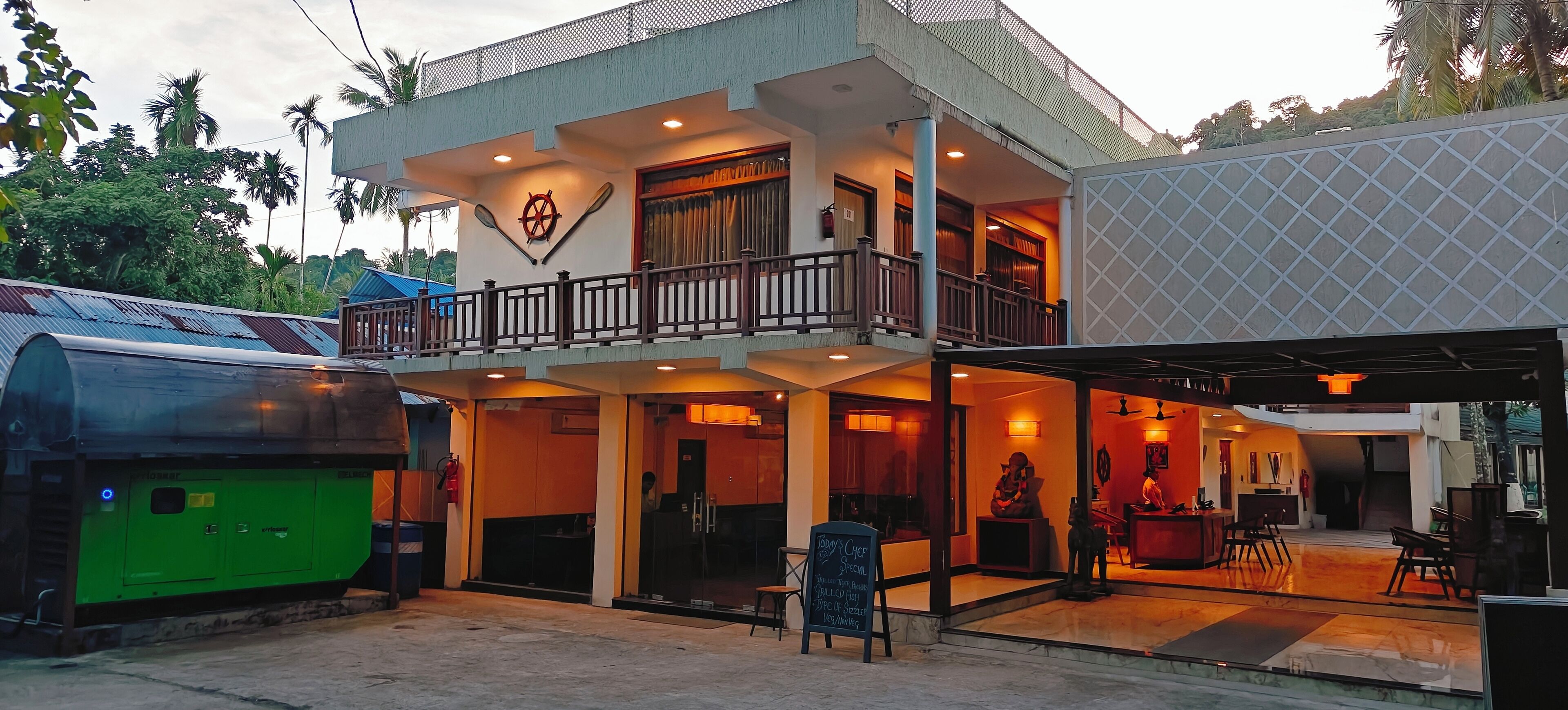 A two-story building with a balcony, a signboard, and a green generator outside.