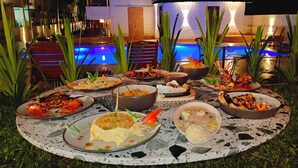 Zona de comedor junto a la piscina, con diversos platos de mariscos y una piscina al fondo.