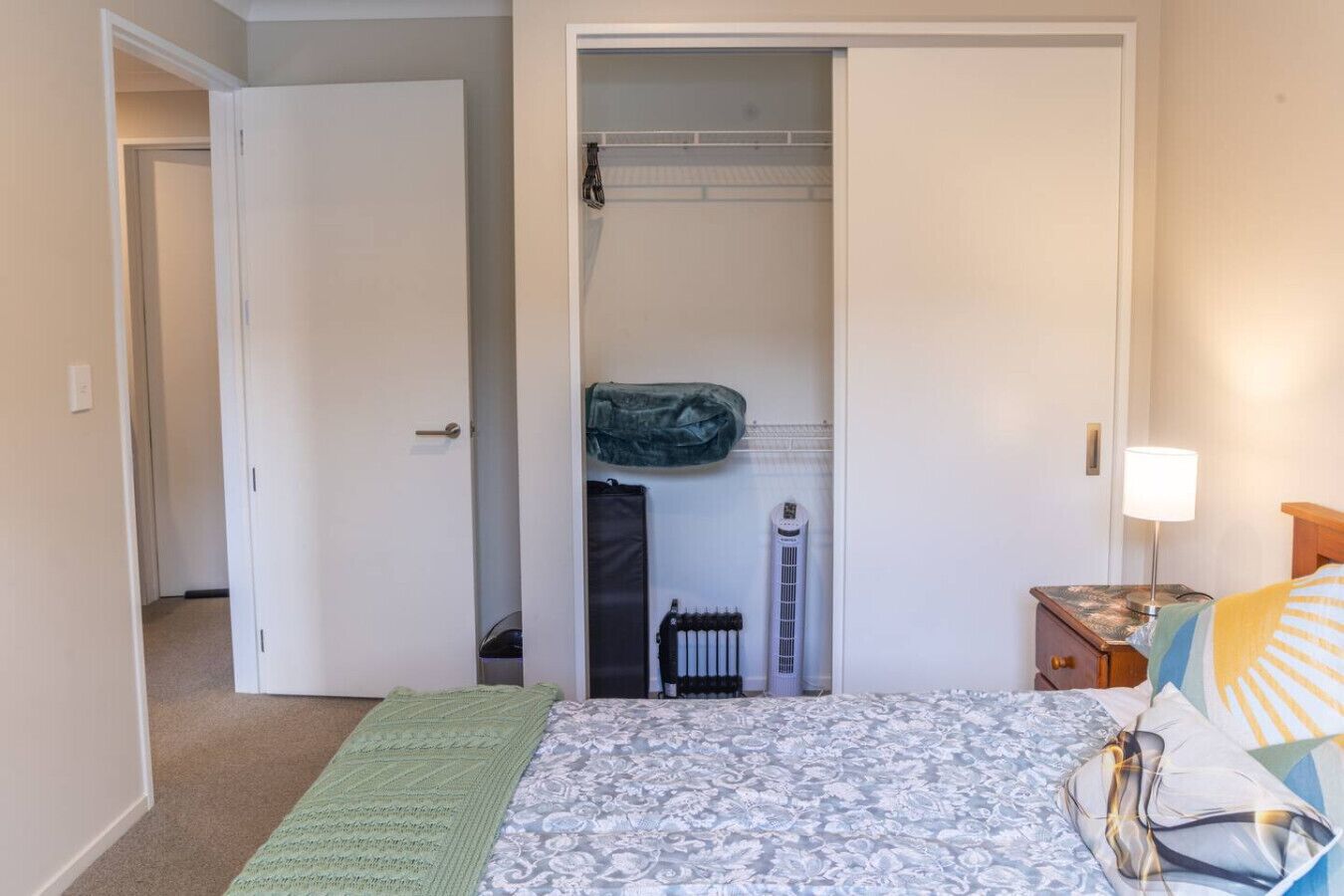 A bedroom with a bed, a nightstand, a lamp, a closet, and a radiator.