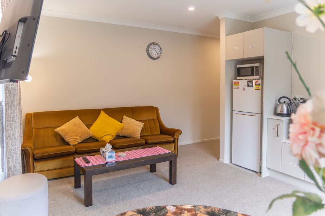 Ein Wohnzimmer mit braunem Sofa, einem Couchtisch und einer Küchenzeile inklusive Kühlschrank und Mikrowelle.