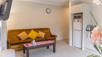 Ein Wohnzimmer mit braunem Sofa, einem Couchtisch und einer Küchenzeile inklusive Kühlschrank und Mikrowelle.