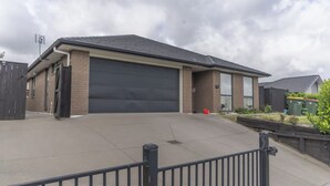 A residential garage with a large black door, a concrete driveway, and a metal fence in the foreground. - New two B/room house  attached to house (Pukekohe)