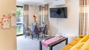 A modern living room with a dining area, a flat-screen TV mounted on the wall, and a yellow sofa. - New two B/room house  attached to house (Pukekohe)