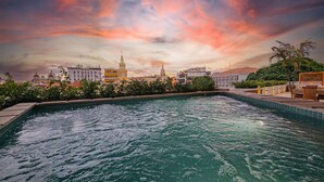 Ein Schwimmbecken mit Stadtansicht im Hintergrund, umgeben von Grünflächen und einem Sonnenuntergangshimmel.