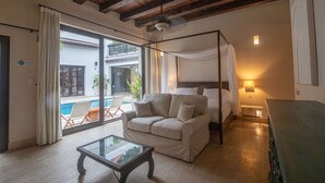 Une chambre avec un lit, un canapé, une table basse en verre et un balcon donnant sur une piscine.
