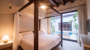 Un lit à baldaquin avec du linge de lit blanc, une table de chevet avec une lampe et une vue sur une piscine, visible à travers une porte vitrée.