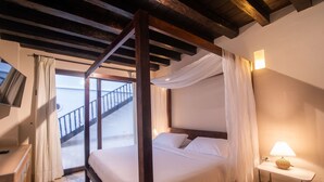 Un lit à baldaquin avec du linge de lit blanc, une table de chevet avec une lampe et une vue sur un balcon doté d’une balustrade.