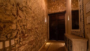Un couloir étroit aux murs de pierre, doté d’un plancher en bois et terminé par une porte en bois sombre.
