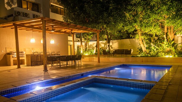 Una piscina con borde de azulejos, rodeada por un porche cubierto con sillas y una mesa.