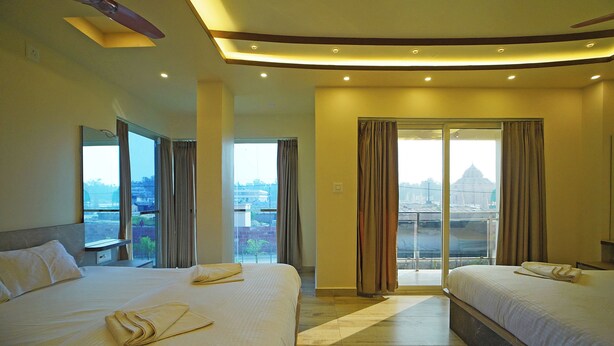 A hotel room with two beds, a large window with curtains, and a view of a cityscape. - Prapti resort (Kanthi)