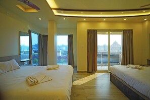 Habitación de hotel con dos camas, un ventanal con cortinas y vistas a un paisaje urbano.