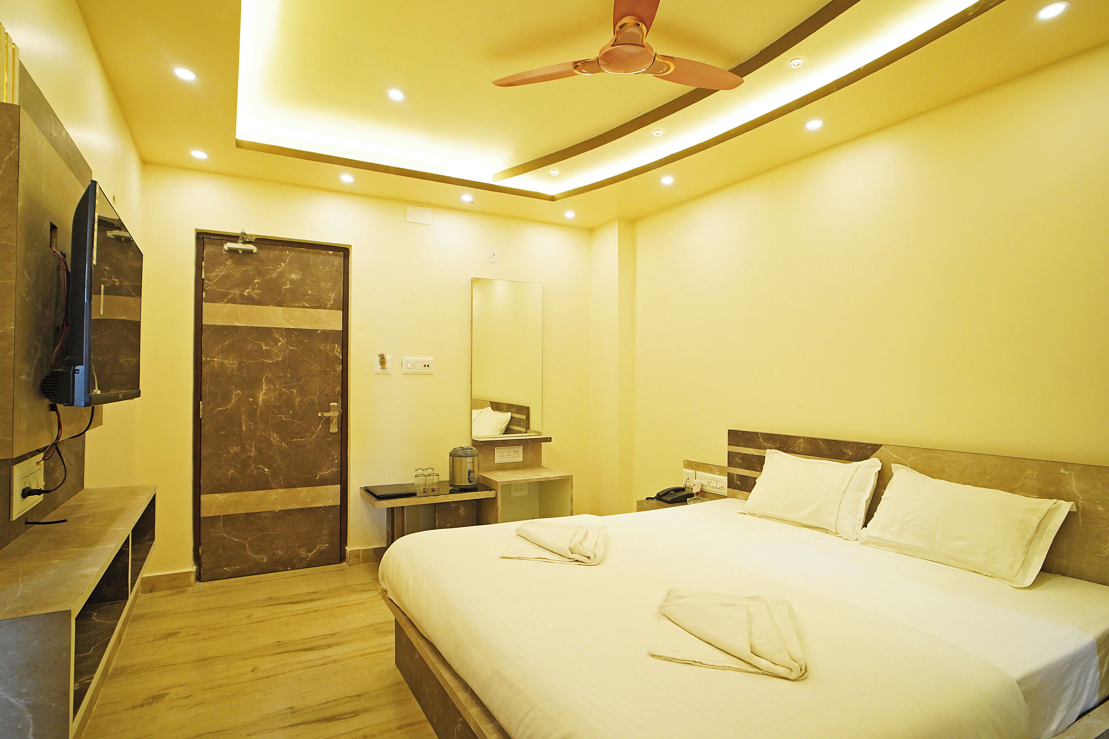 A hotel room with a bed, bedside table, mirror, and ceiling fan.