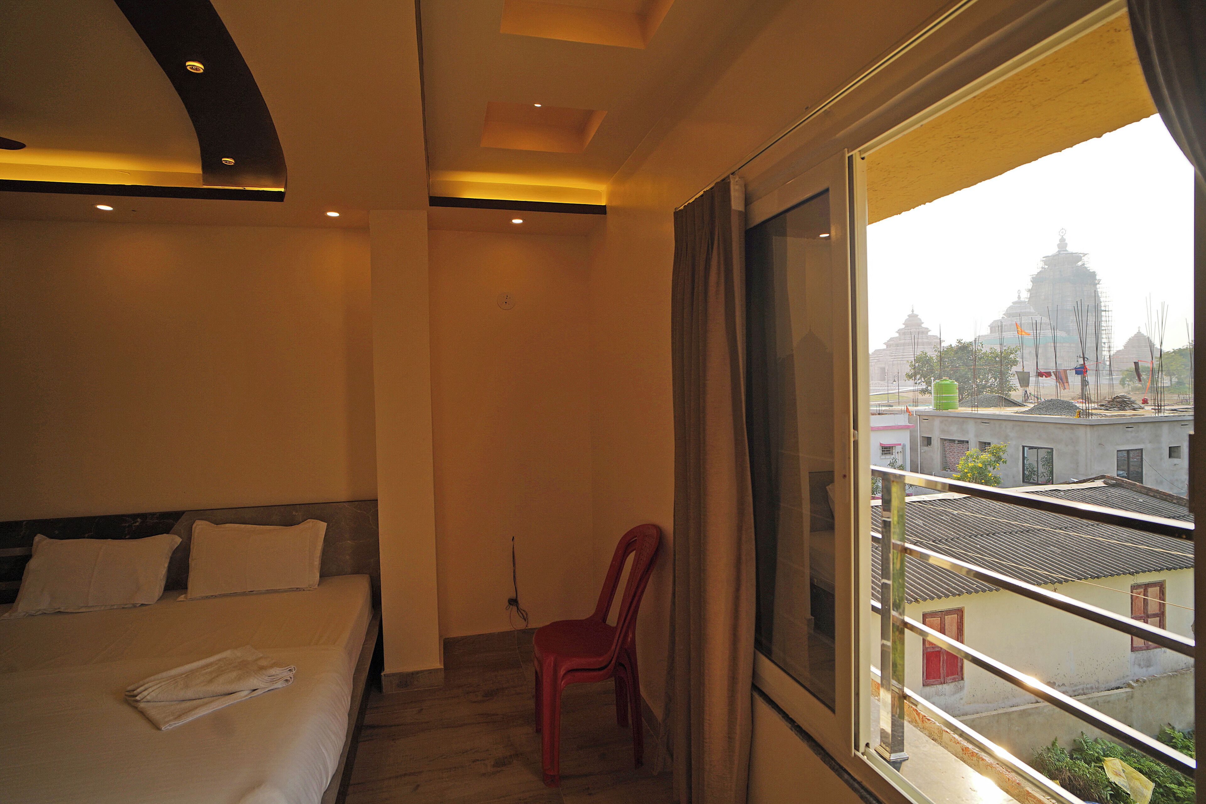 Habitación de hotel con cama, una silla roja y un ventanal que ofrece vistas a edificios y un templo.