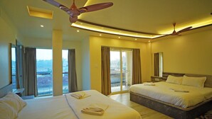 A hotel room with two beds, a ceiling fan, and a view of the city through large windows. - Prapti resort (Kanthi)