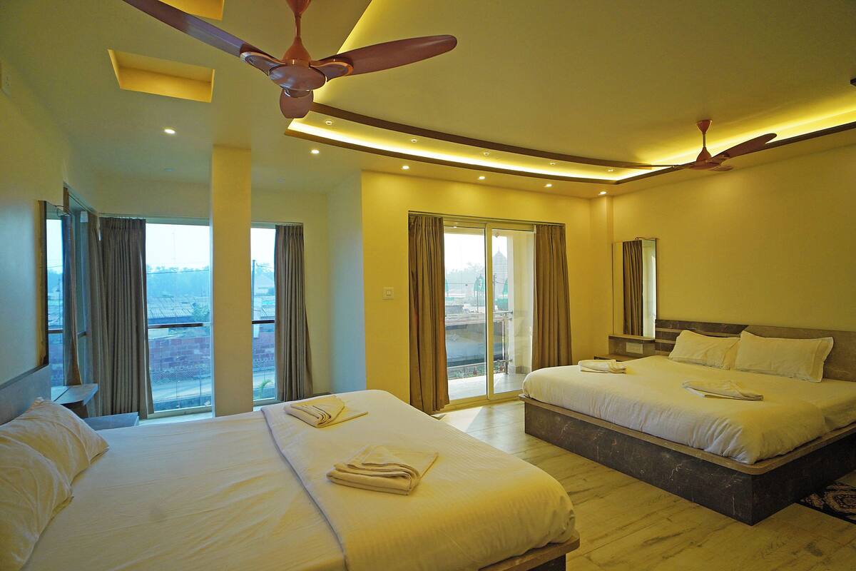 A hotel room with two beds, a ceiling fan, and a view of the city through large windows.