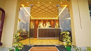 A reception area with a wooden counter, glass doors, and potted plants. - Prapti resort (Kanthi)