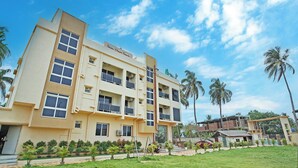 A multi-story hotel with a flat roof, balconies, and a well-maintained lawn with palm trees. - Prapti resort (Kanthi)