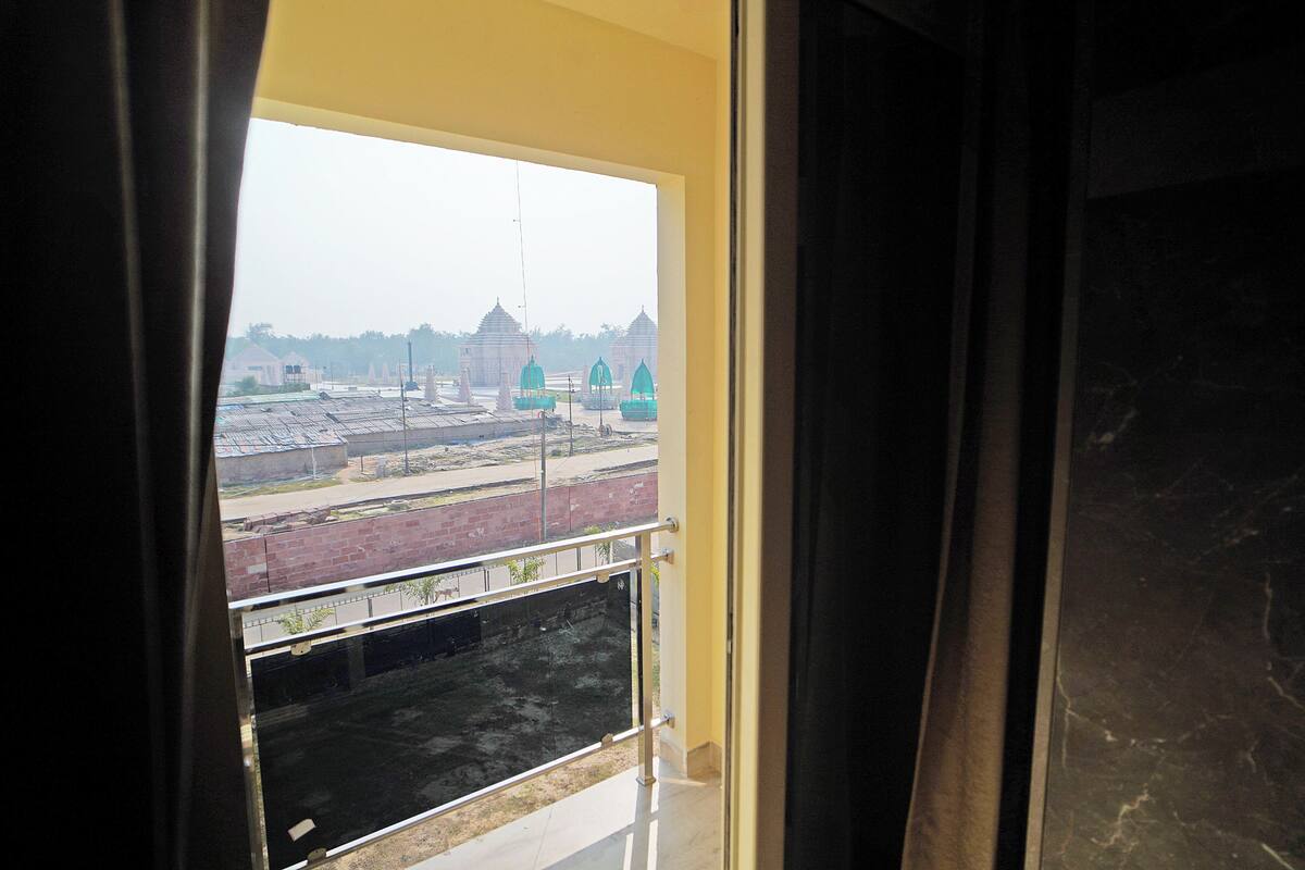 A view through a window with a metal railing, looking out to a construction site with buildings and a brick wall.