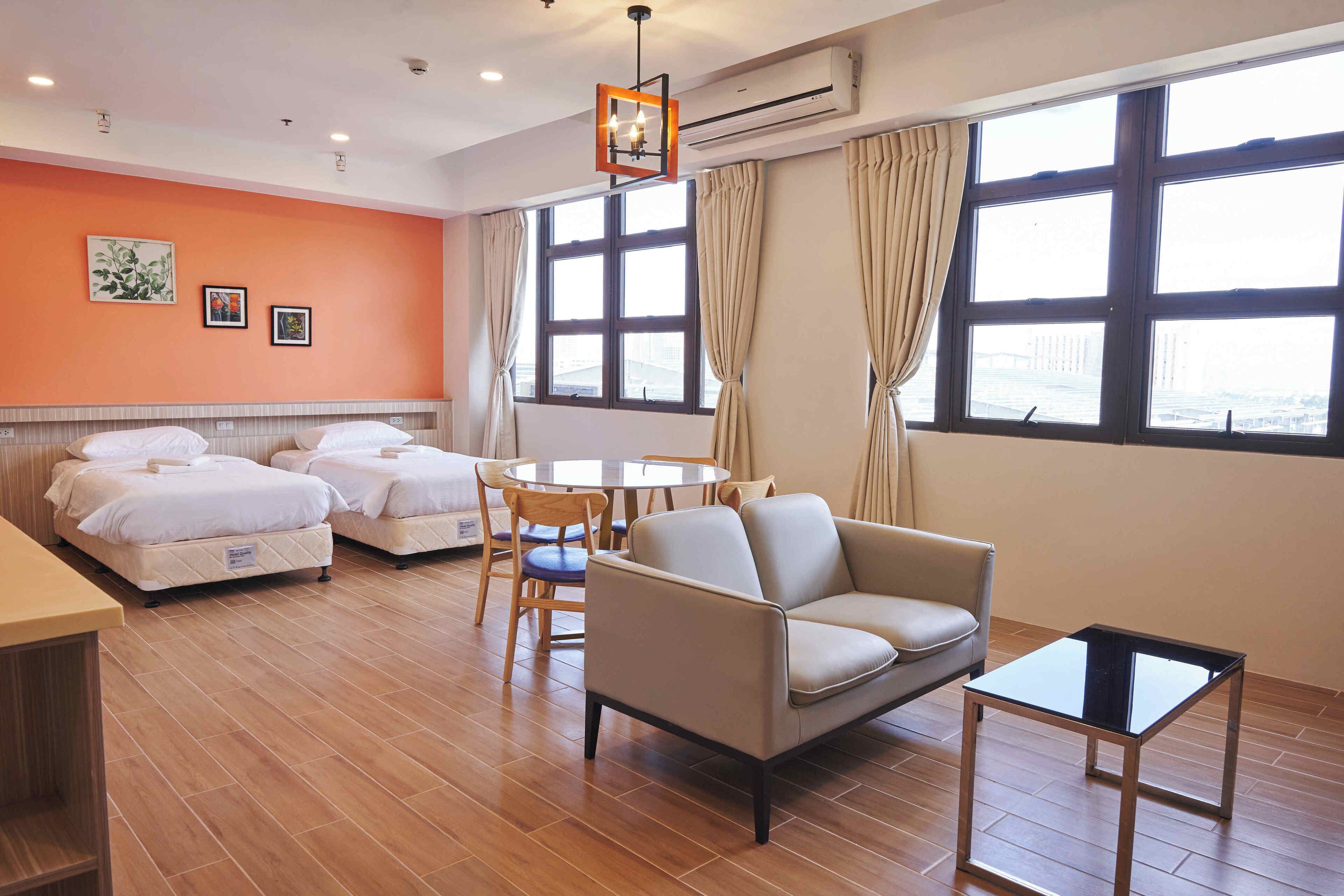 A hotel room with two beds, a sofa, a small table, and a view of the city through large windows.