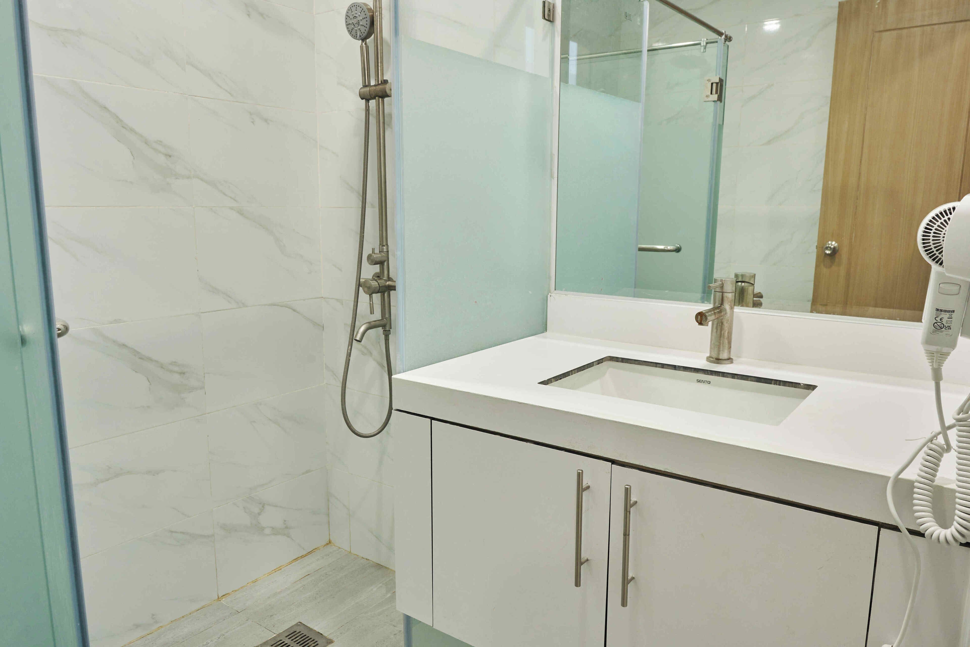 Un baño moderno con cabina de ducha de vidrio, un lavabo blanco y un secador de pelo sobre la encimera.