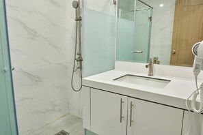 A modern bathroom with a glass shower enclosure, a white sink, and a hairdryer on the counter. - Treewoods Residences (Cebu City)