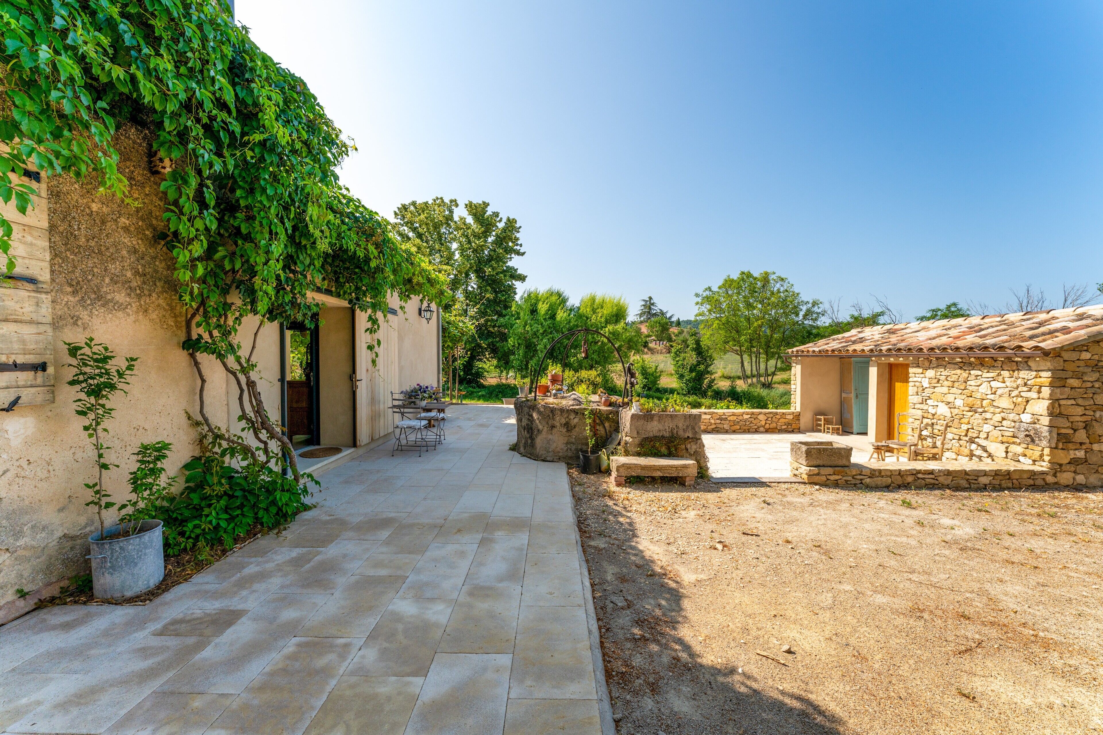 A courtyard with a stone building, a paved walkway, and a small table with chairs.