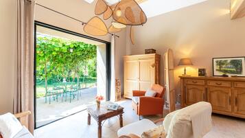 A spacious living room with a large sliding glass door leading to a garden, a wooden cabinet, a sofa, and a table with a lamp.