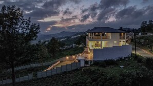 Een modern huis met twee verdiepingen en een balkon, gelegen op een heuvel met uitzicht op het omliggende landschap.