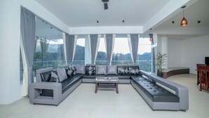 Een moderne woonkamer met een royale modulaire bank, een plafondventilator en grote ramen met uitzicht op bergen.