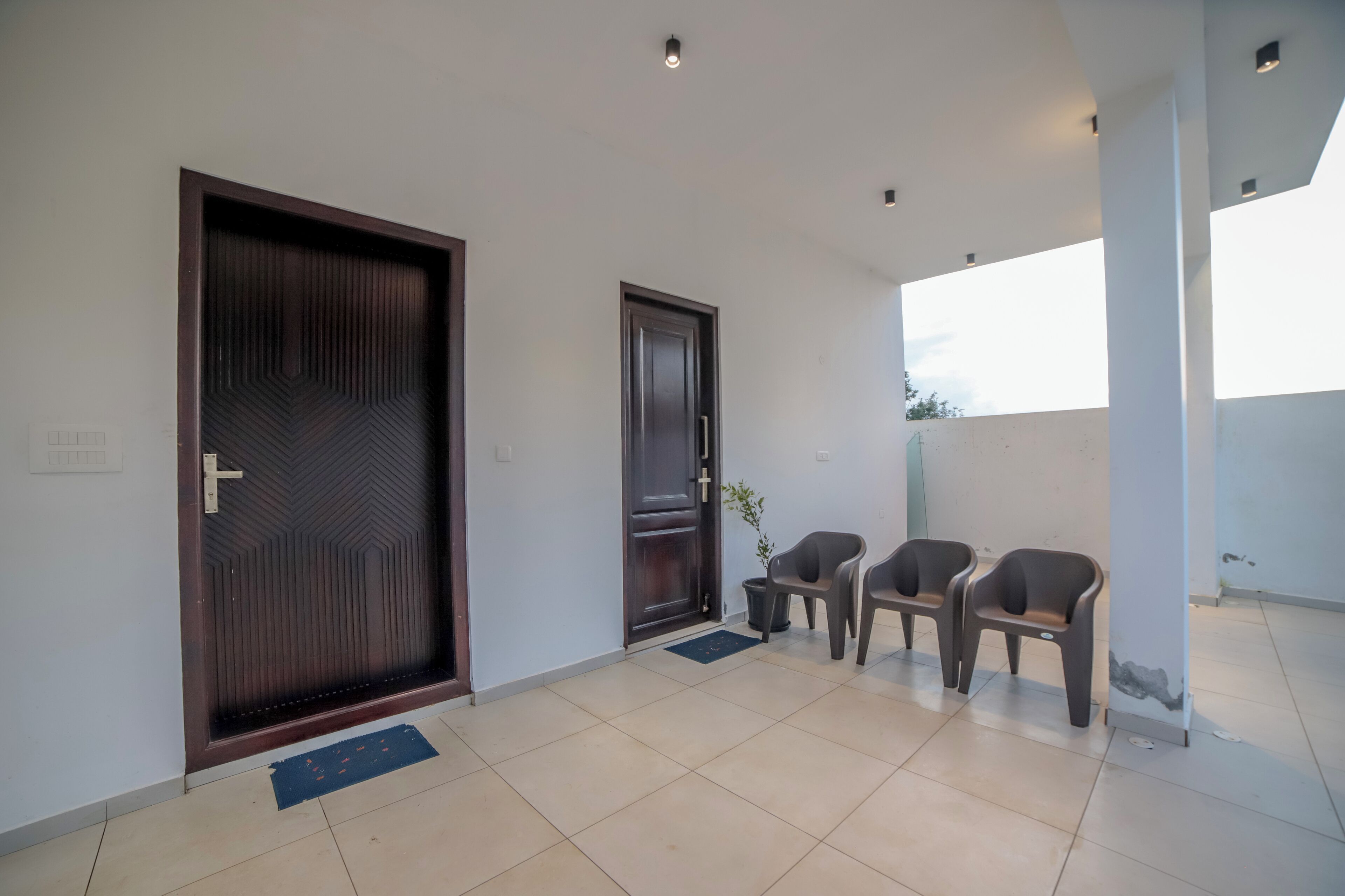 A hallway with a large wooden door, a smaller door, and two plastic chairs.
