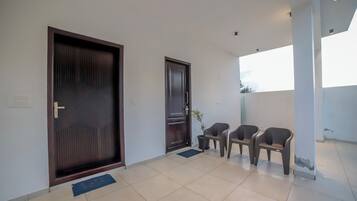 A hallway with a large wooden door, a smaller door, and two plastic chairs.