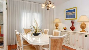 Un coin repas comprenant une table blanche, des chaises, un lustre et un meuble avec des tiroirs.
