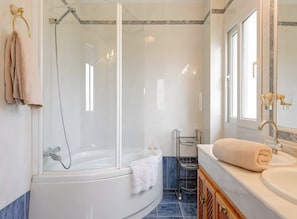 A modern bathroom with a glass-enclosed shower, a white bathtub, a vanity with a sink, and a towel rack.