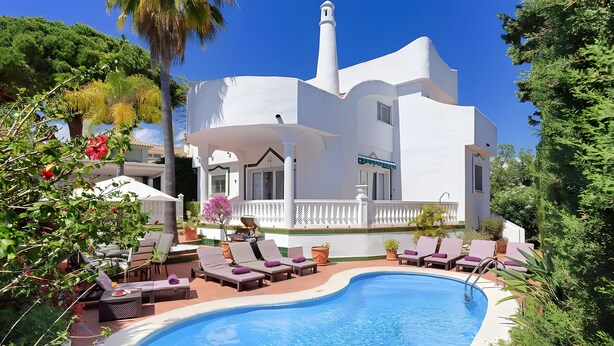Un bâtiment blanc avec une piscine, des chaises longues et une clôture blanche.