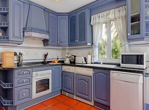 Eine Küche mit blauen Schränken, einer Mikrowelle und einem Fenster mit Vorhängen.