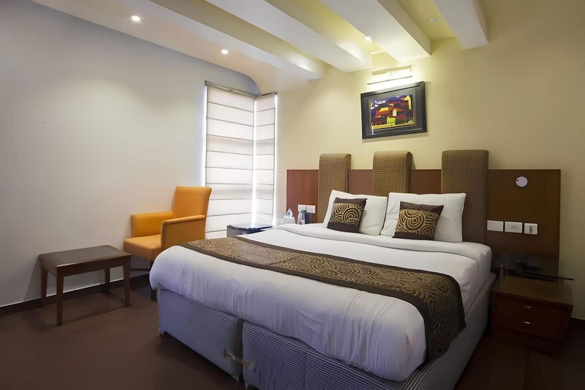 A hotel room with a large bed, a chair, a bedside table, and a nightstand.