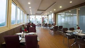 A modern restaurant with high ceilings, large windows, and a view of the cityscape. - HOTEL PALM D'OR (New Delhi)