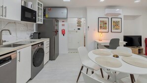 A modern kitchen with a built-in washing machine, a microwave, and a refrigerator. There is a dining area with a white table and chairs.