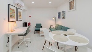 A modern, well-lit room with a white desk, teal chair, and a round table with placemats. There are framed pictures on the walls and a fire extinguisher visible.