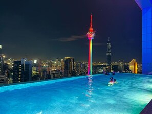 Ein Pool auf dem Dach mit Stadtansicht im Hintergrund, darunter ein markanter Turm mit farbenfroher Lichtshow.
