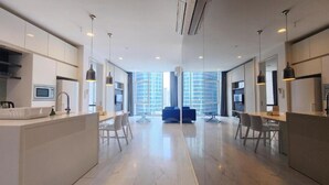 A modern kitchen with a central island, a dining area with a blue sofa, and large windows offering a city view. - The Platinum Suites KLCC by Moonlight (Kuala Lumpur)